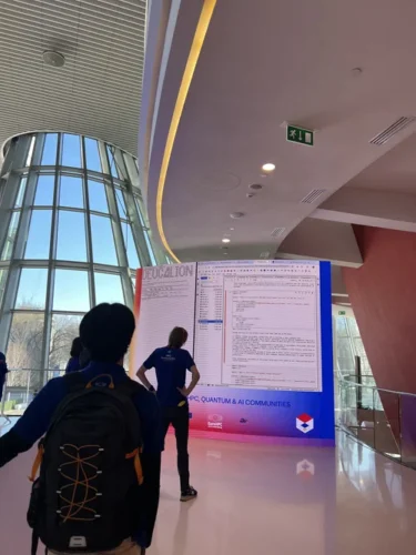 People standing in a modern building lobby, looking at a large screen displaying code and Deucalion-related content, with natural light coming through a curved glass wall.