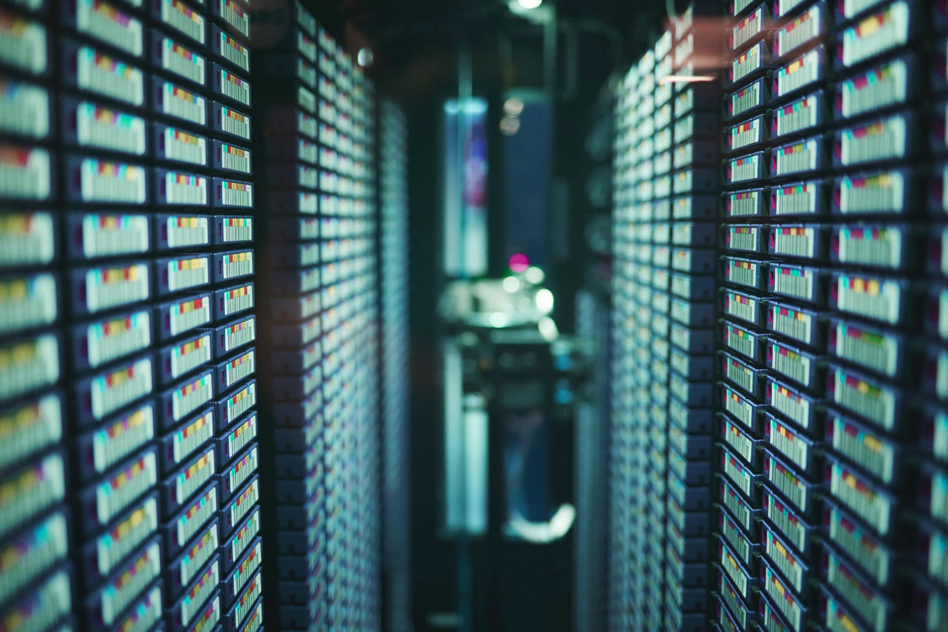 Close-up view down a narrow data centre aisle with densely packed storage units or tape cartridges on both sides, illuminated with soft, cool lighting and shallow depth of field.