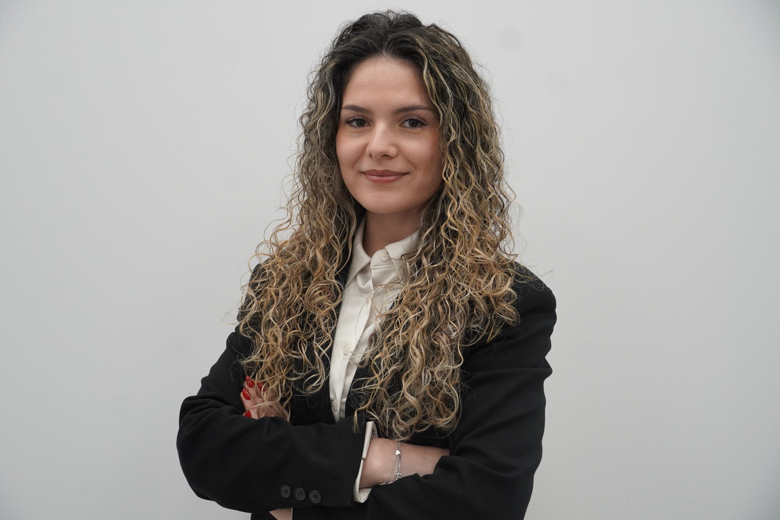 Woman wearing a white shirt and a black blazer with arms-crossed.