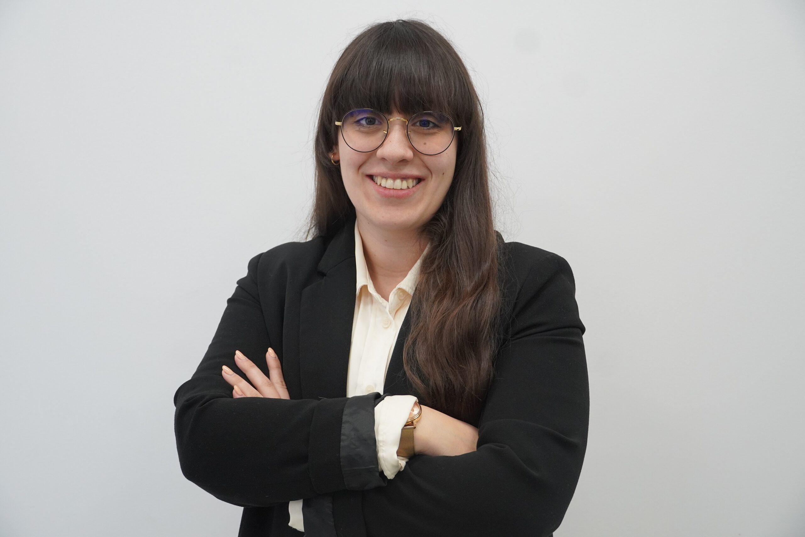 Woman wearing a bege shirt and a black blazer with arms-crossed.