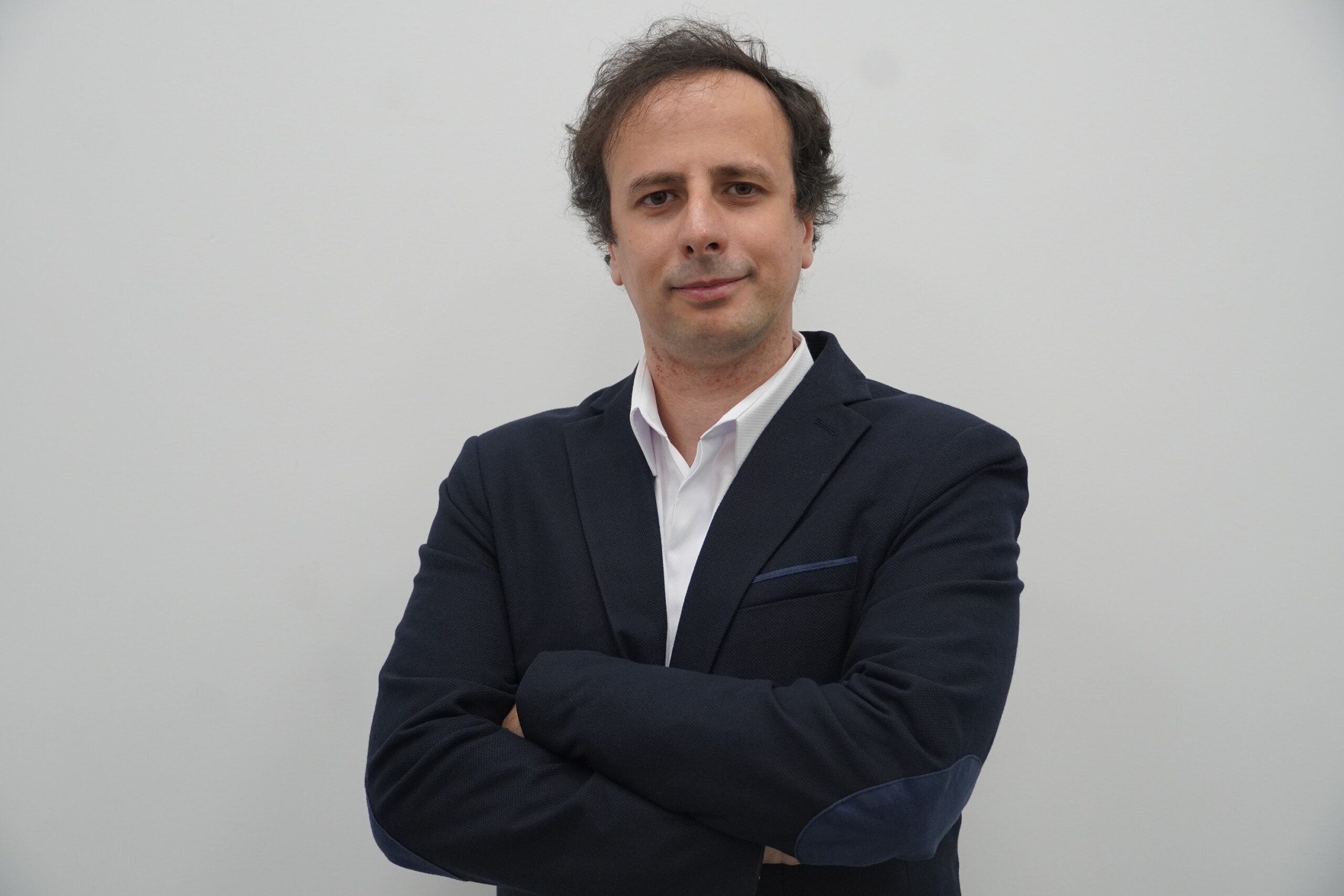 Man wearing a white shirt and a black blazer with arms-crossed.