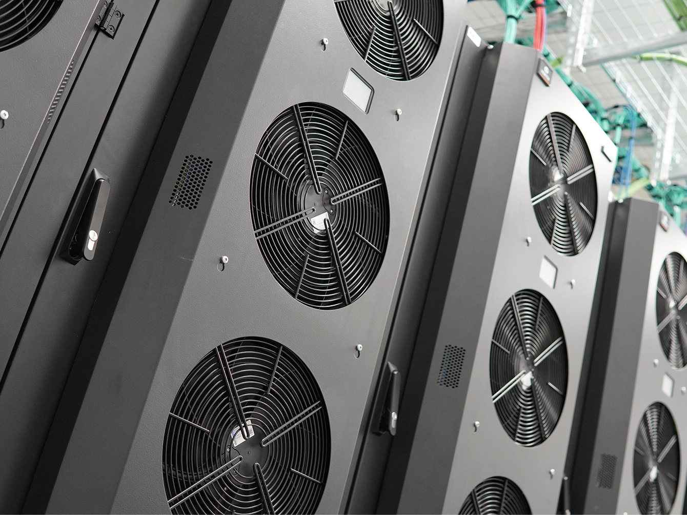Close-up of industrial cooling units with multiple large fans, part of a data centre infrastructure, with visible cabling and ventilation systems in the background.