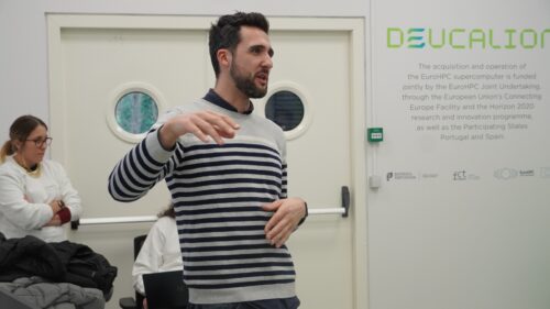 Male researcher talking in a room with another researcher at the back and with information about the Deucalion supercomputer in one of the walls.