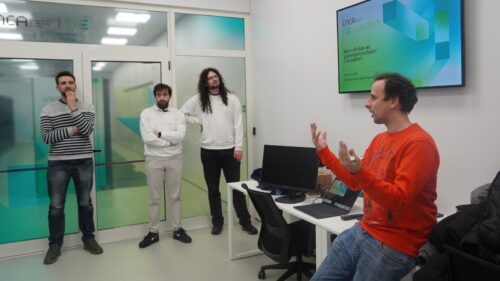 Four male researchers talking in a room with a screen with Deucalion logo.