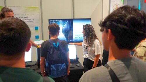 Researchers and students gathered at the Deucalion stand while a scientific demonstration is explained, with screens displaying computational visualisations.