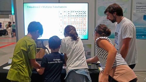 Children and a facilitator interact with a digital display at the Deucalion stand, exploring parallel computing concepts through a hands-on educational activity.