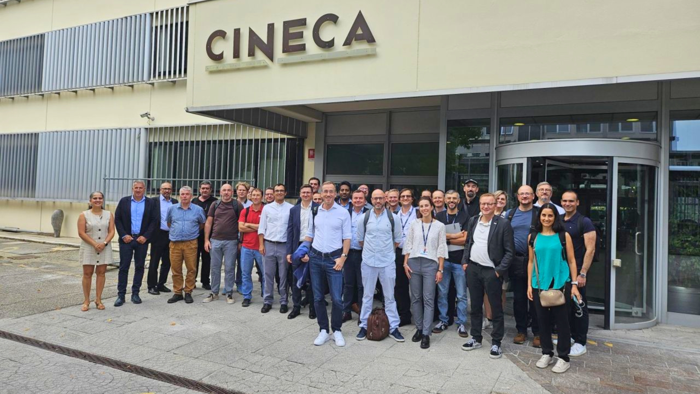 Group photo of researchers and HPC professionals gathered outside the CINECA headquarters, standing in front of the building entrance.