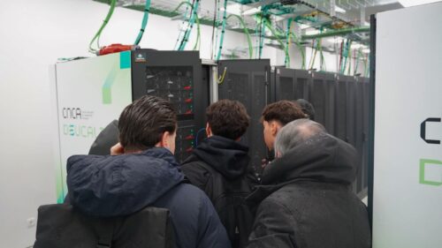 Um investigador explica a infraestrutura do supercomputador a um pequeno grupo de visitantes em frente a um armário de computadores aberto.
