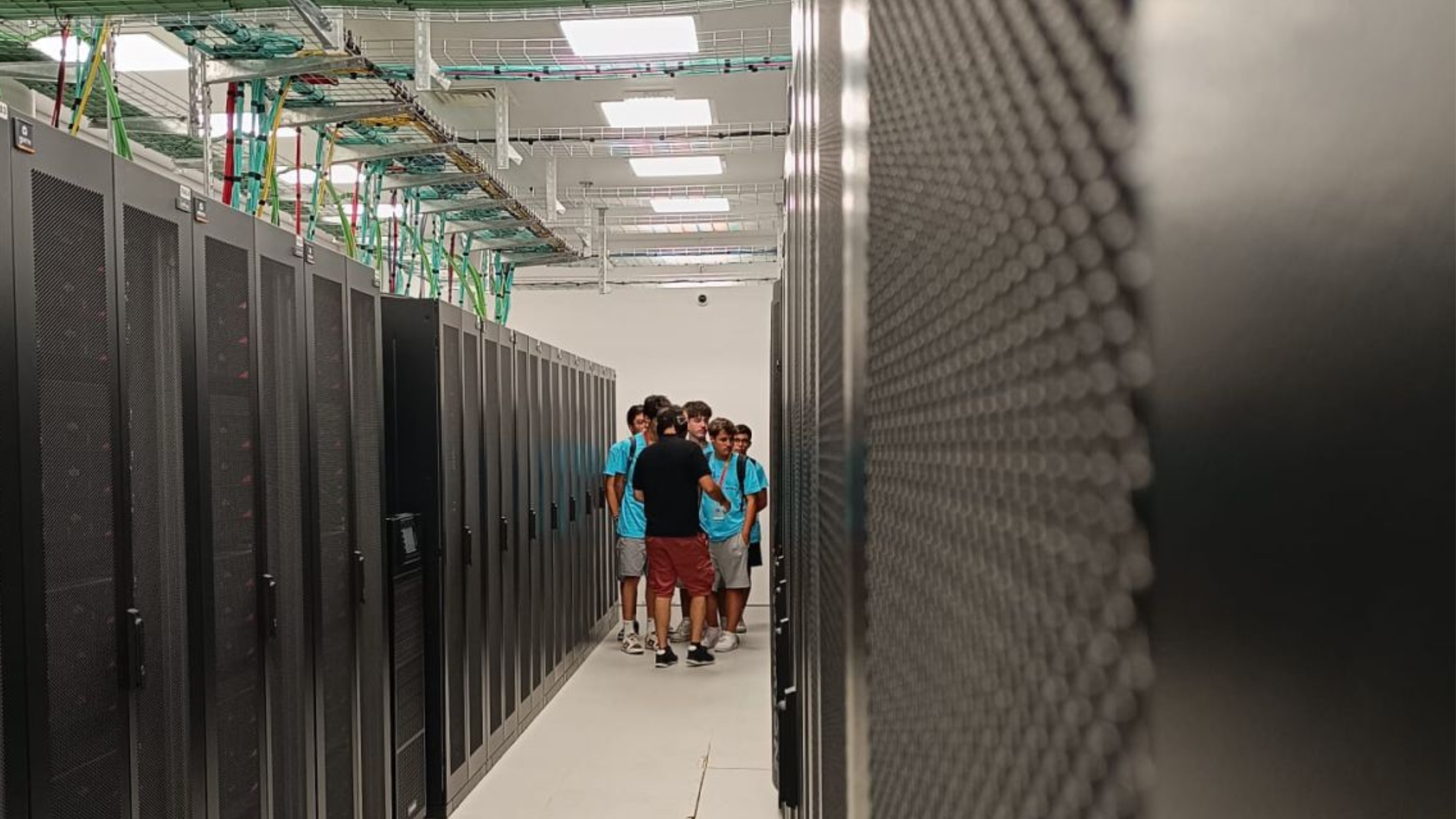 Group of students visiting a high-performance computing data centre, walking between server racks during a guided tour.