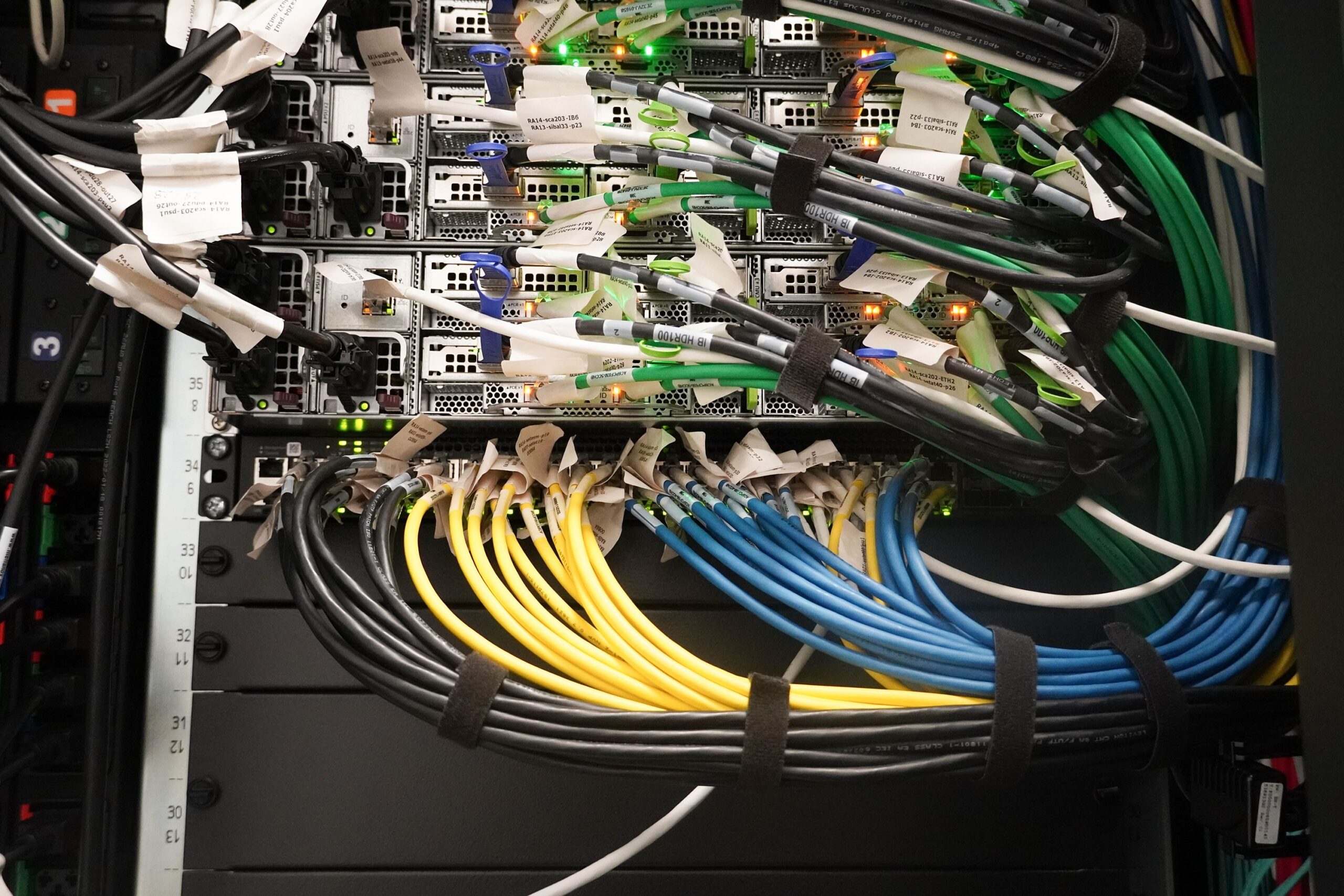 Close-up of network equipment in a data centre showing multiple labelled cables in different colours connected to server ports with blinking indicator lights.