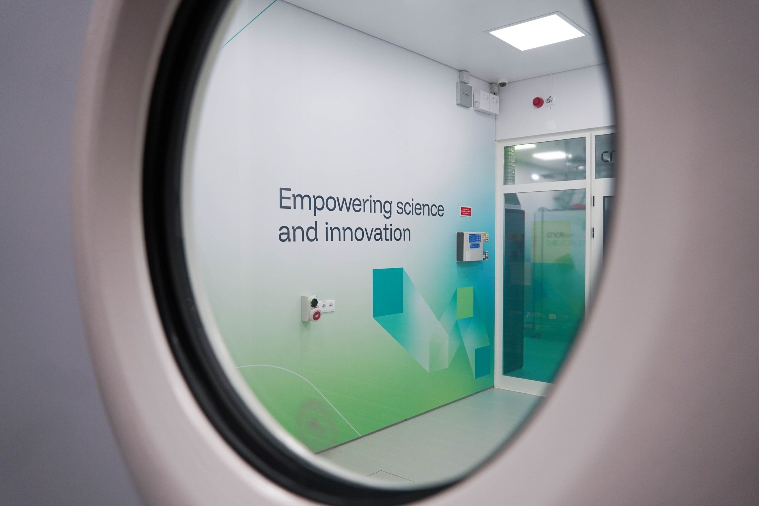 Reflection of the Deucalion facility entrance and the phrase “Empowering science and innovation” seen through a circular wall mirror.
