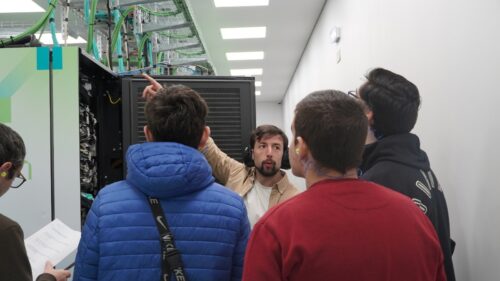 Investigador a explicar os componentes de um rack de servidor a um pequeno grupo de estudantes dentro de um centro de dados de supercomputação.