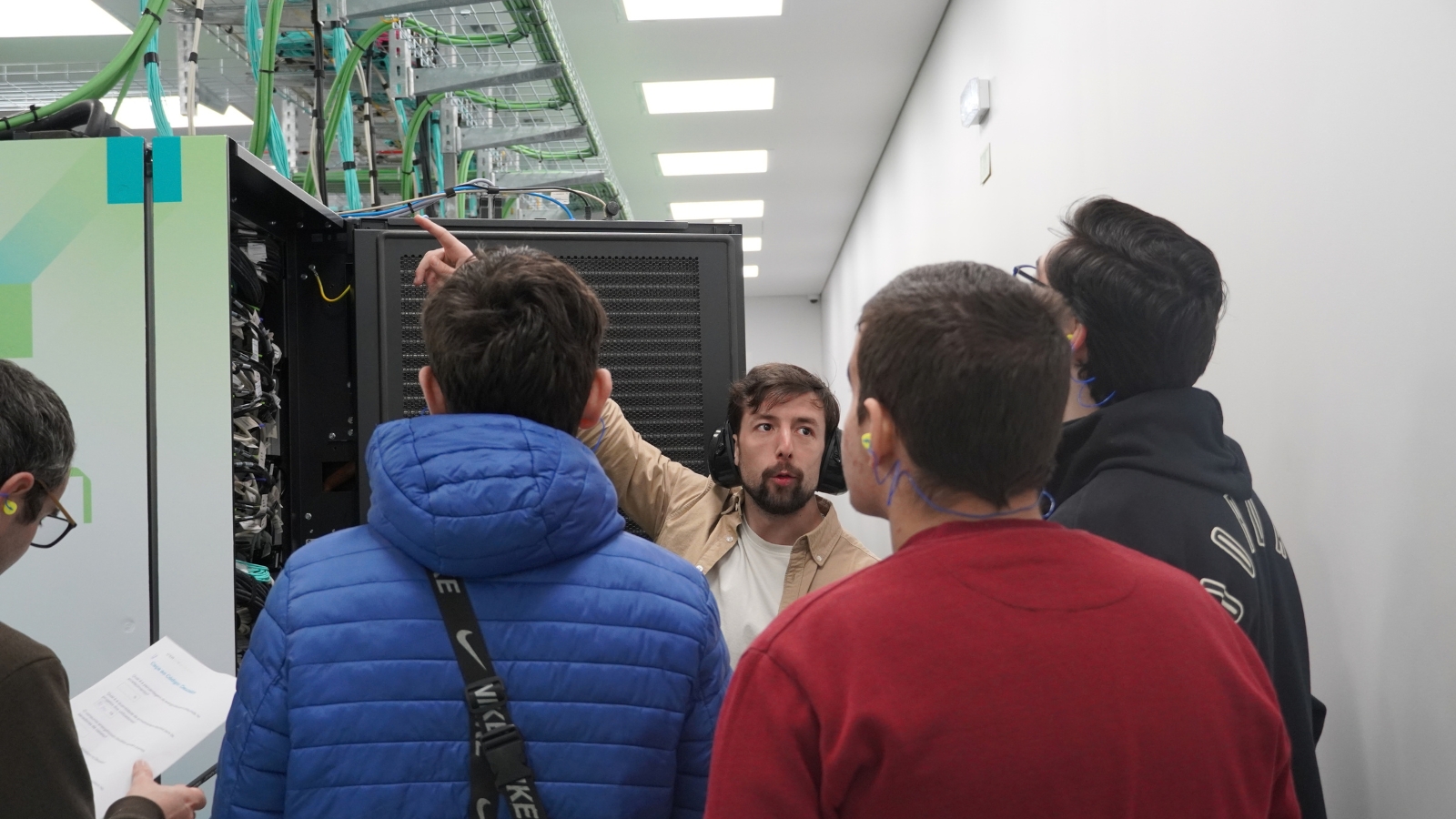 Researcher explaining the components of a server rack to a small group of students inside a supercomputing data centre.