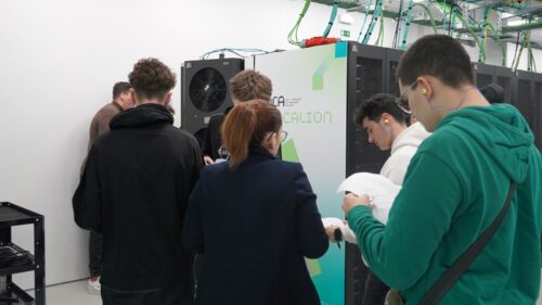 Group of students visiting a supercomputing facility, standing beside a Deucalion server cabinet while examining printed materials during a guided tour.