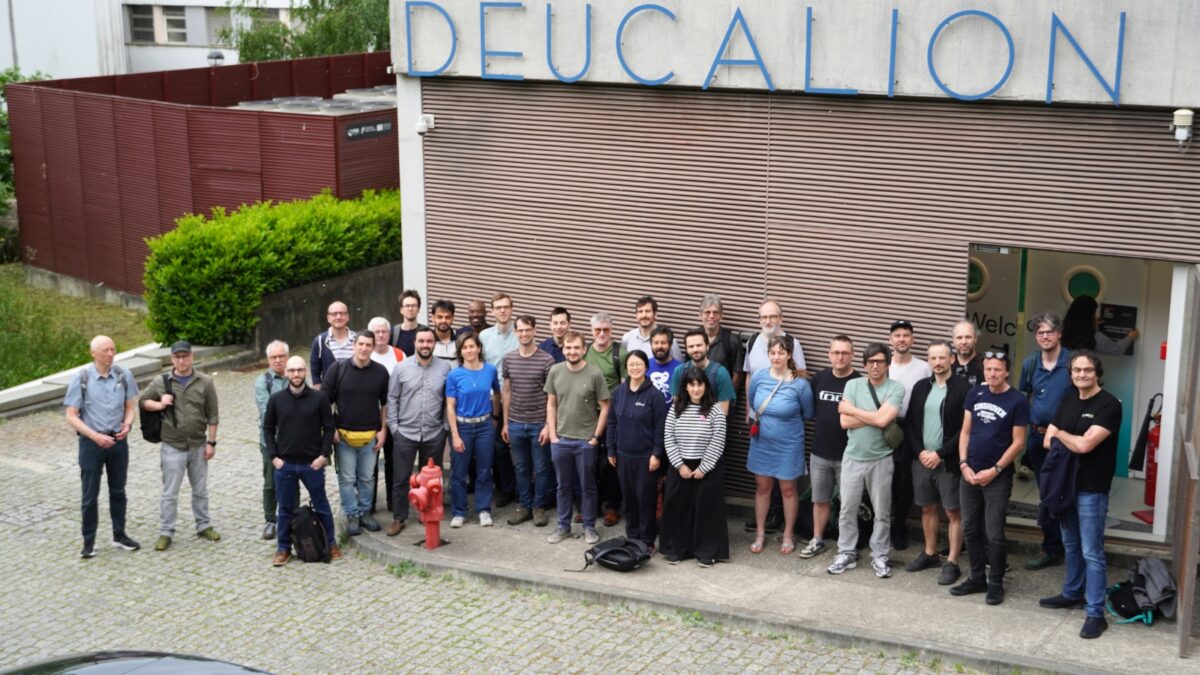 Um grande grupo de participantes do evento em pé na relva em frente a um castelo histórico de pedra.