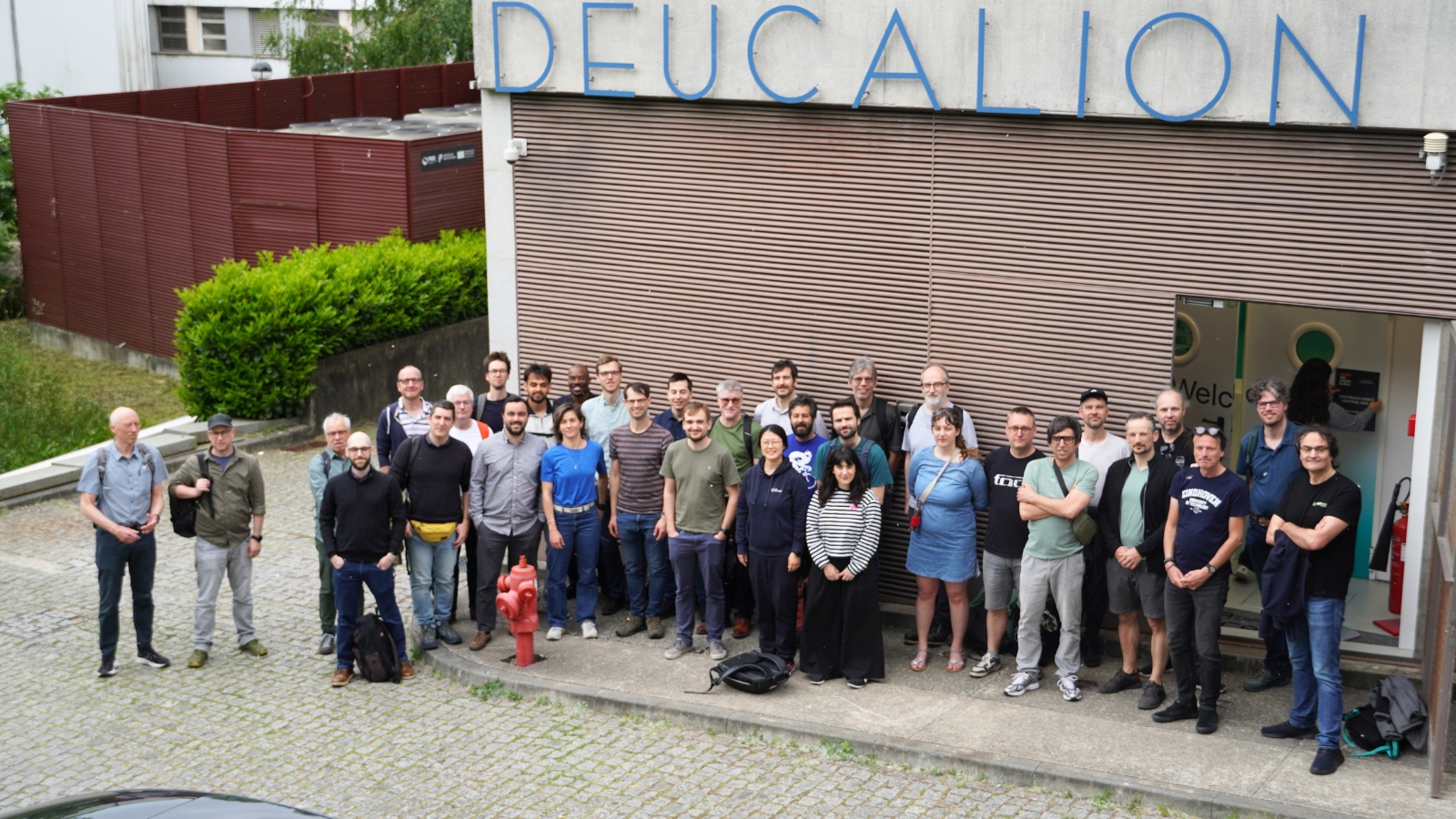 Fotografia de grupo dos participantes em frente a um edifício com a inscrição "Deucalion"