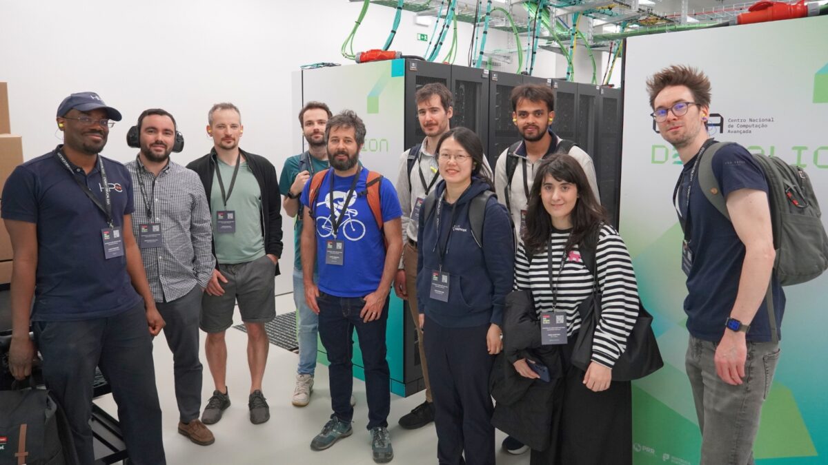 Grupo de participantes a posar dentro de um centro de dados junto a racks de servidores.