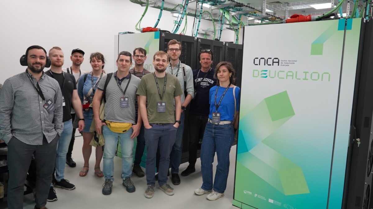 Grupo de participantes a posar no interior de um centro de dados, junto aos racks do sistema Deucalion, com crachás, durante uma visita às instalações de HPC.