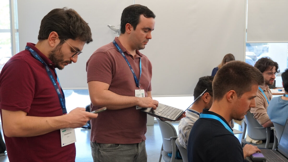 Participantes a trabalhar em computadores portáteis e tablets, enquanto outros estão focados a trabalhar nas suas mesas, durante um workshop de HPC.
