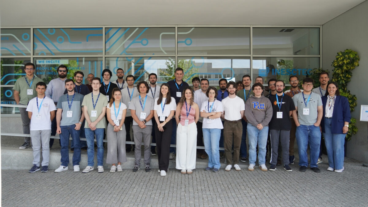 Grupo de participantes a posar para uma foto no exterior do edifício do iNESC TEC, a usar a credencial de um evento ao pescoço.