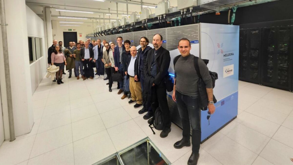 Grupo de participantes ao lado de um supercomputador dentro de um centro de dados, durante uma visita às infraestruturas europeias de HPC.