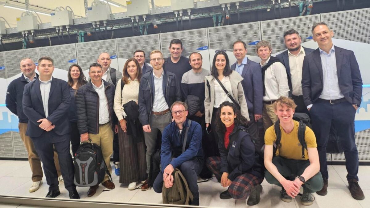 Grupo de participantes a posar em frente a um supercomputador dentro de um centro de dados, durante uma reunião de entidades europeias de alojamento de HPC.