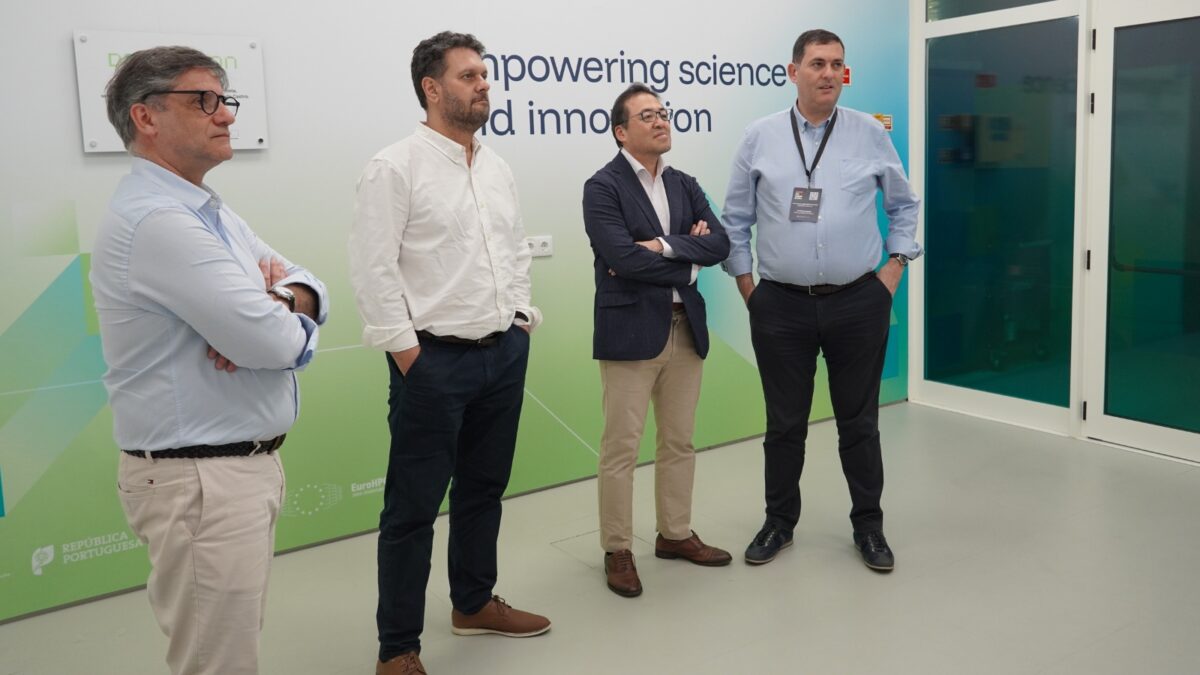 Quatro homens de pé durante uma visita técnica ao Deucalion, enquanto ouvem uma apresentação numa sala.