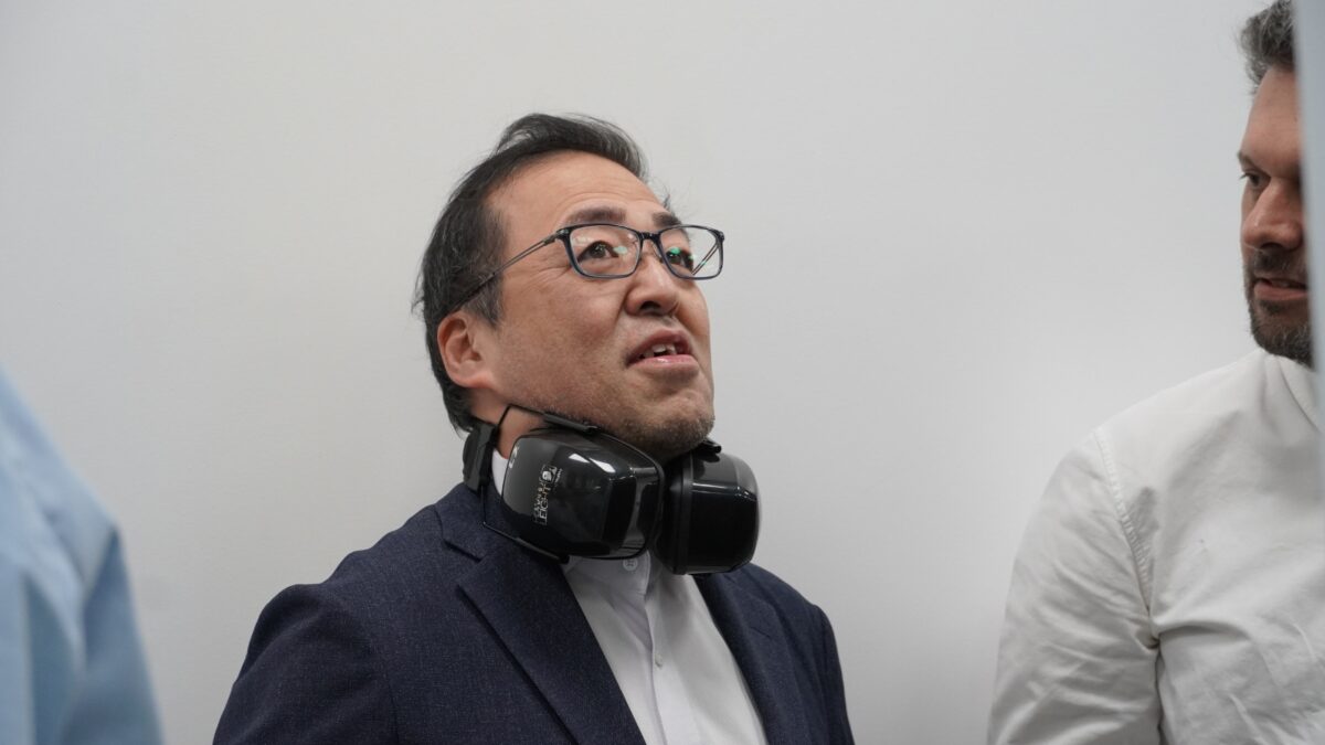 Representante da Fsas Technologies com auscultadores de proteção dos ouvidos ao pescoço durante uma visita técnica a uma infraestrutura de computação avançada.
