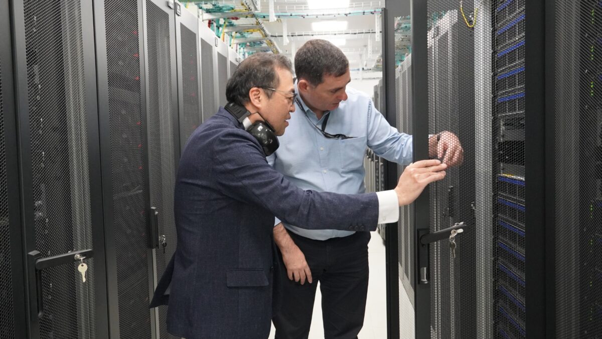 Dois homens a ver as racks de servidores de um supercomputador durante uma visita técnica.