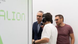 Two male visitors wear hearing protection while receiving a guided explanation inside the Deucalion supercomputer facility during a technical tour.