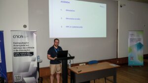 A speaker delivers a presentation on simulation, HPC, and cybersecurity at a CNCA event, standing at the podium beside the projected agenda.