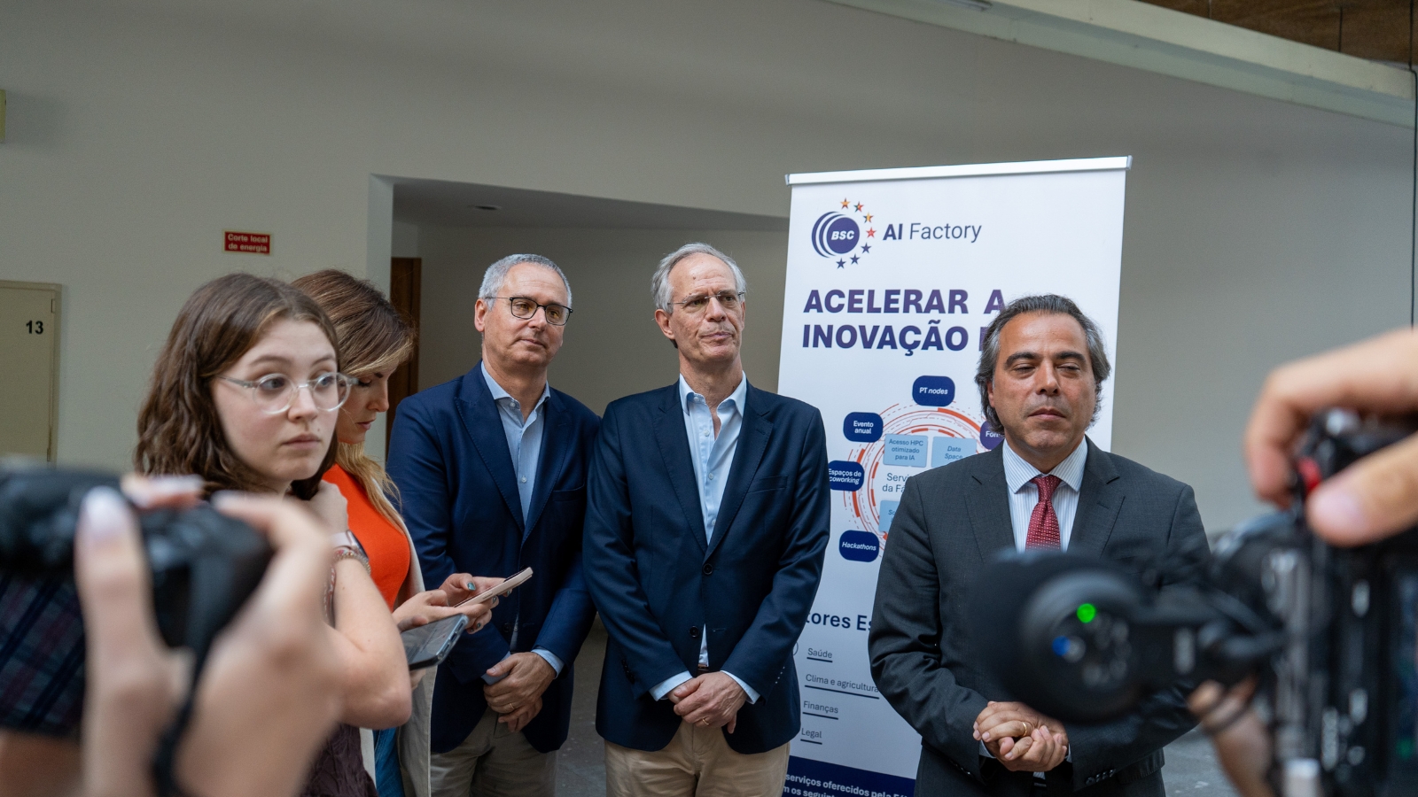 Rpresentatives from the BSC AI Factory and Foundation for Science and Technology and the Mayor of Guimarães speak with members of the press during a media briefing. Journalists gather around with cameras while the speakers stand beside a banner highlighting the BSC AI Factory.