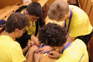 Quatro estudantes, vestidos com t-shirts amarelas, colaboram numa atividade de construção com LEGO numa secretária de uma sala de aula da universidade.